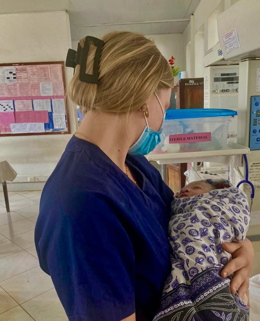 Volunteer nurse in scrubs holding a newborn at Kaloleni Hospital